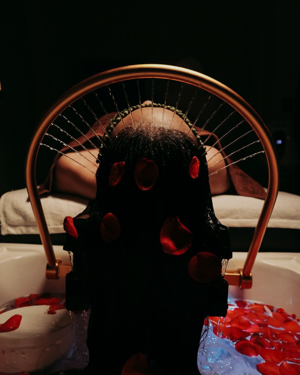 Korean head spa: water cascading through hair over a basin scattered with rose petals.